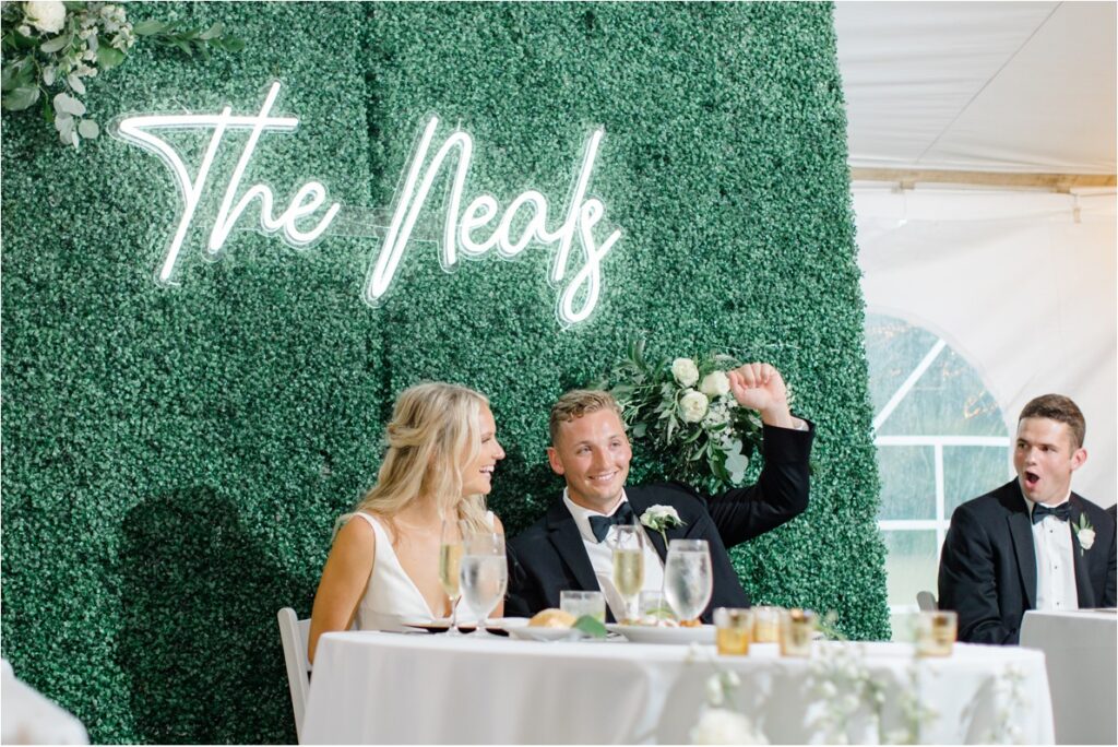 A couple sitting at the head table of their wedding reception looking excited.