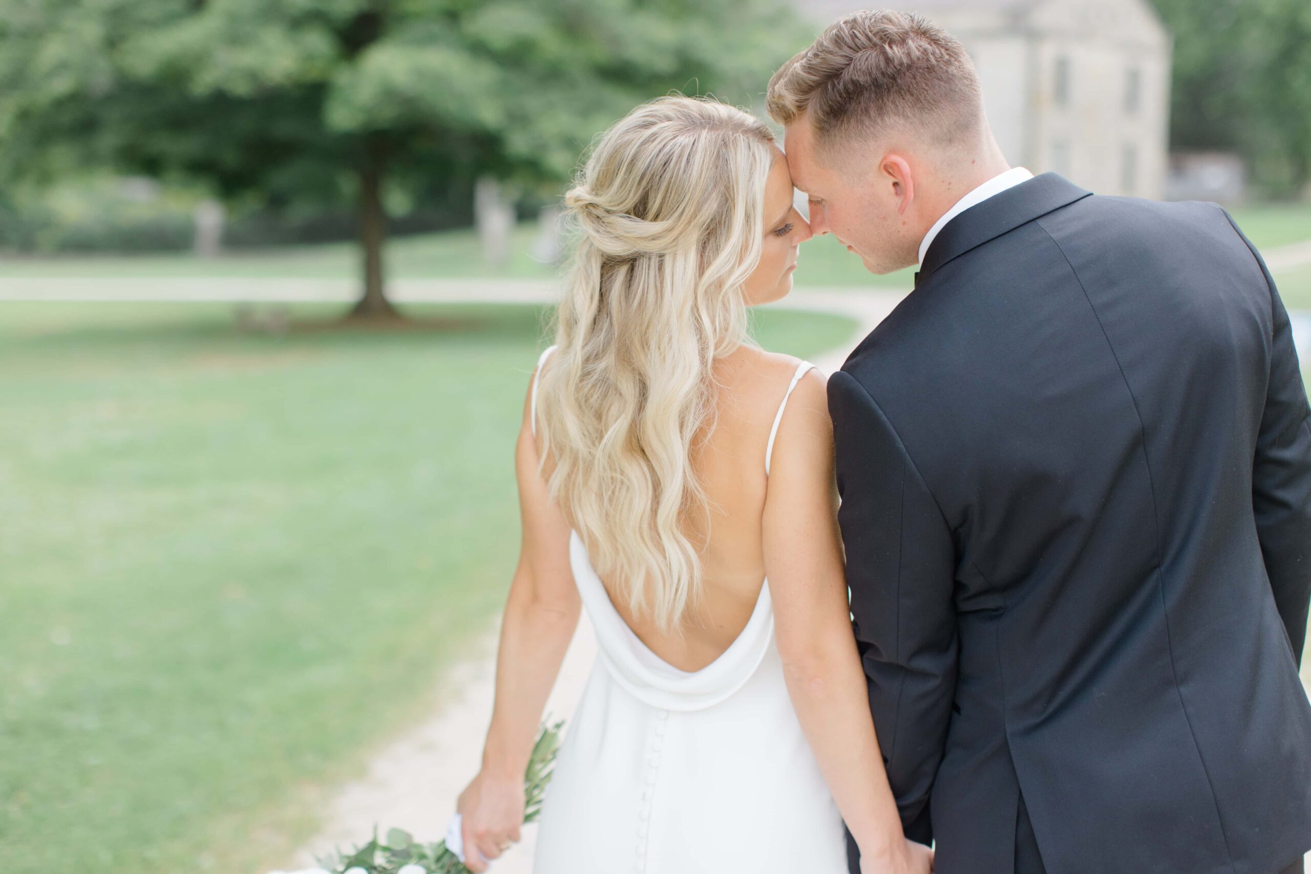 A bride and groom touching foreheads as their backs are two the camera