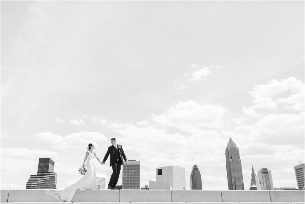 A couple walking with the Cleveland skyline behind them during their wedding photo session.