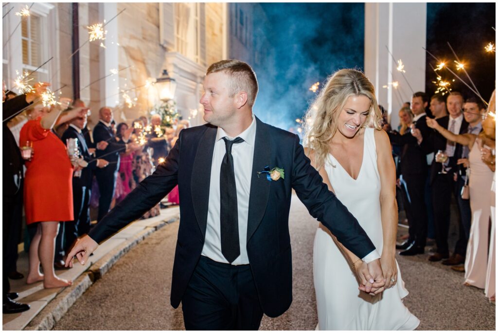A couple doing their grand exit from their wedding reception surrounded by guests holding sparklers.