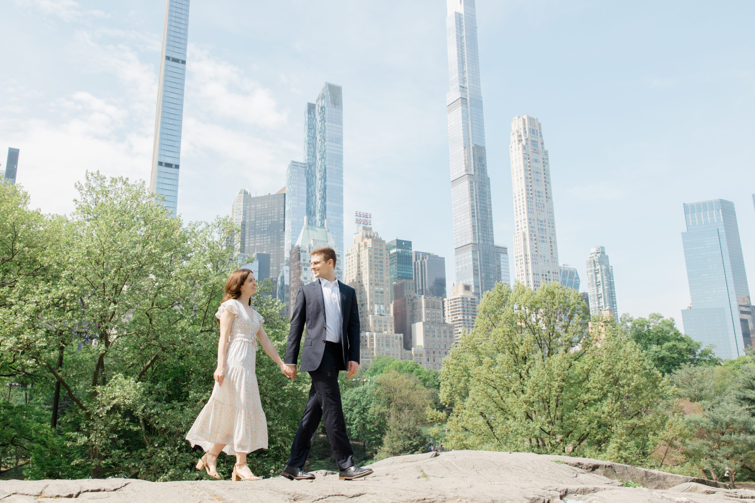An engaged couple walking together and holding hands on top of a rock formation in Central Park in New York City