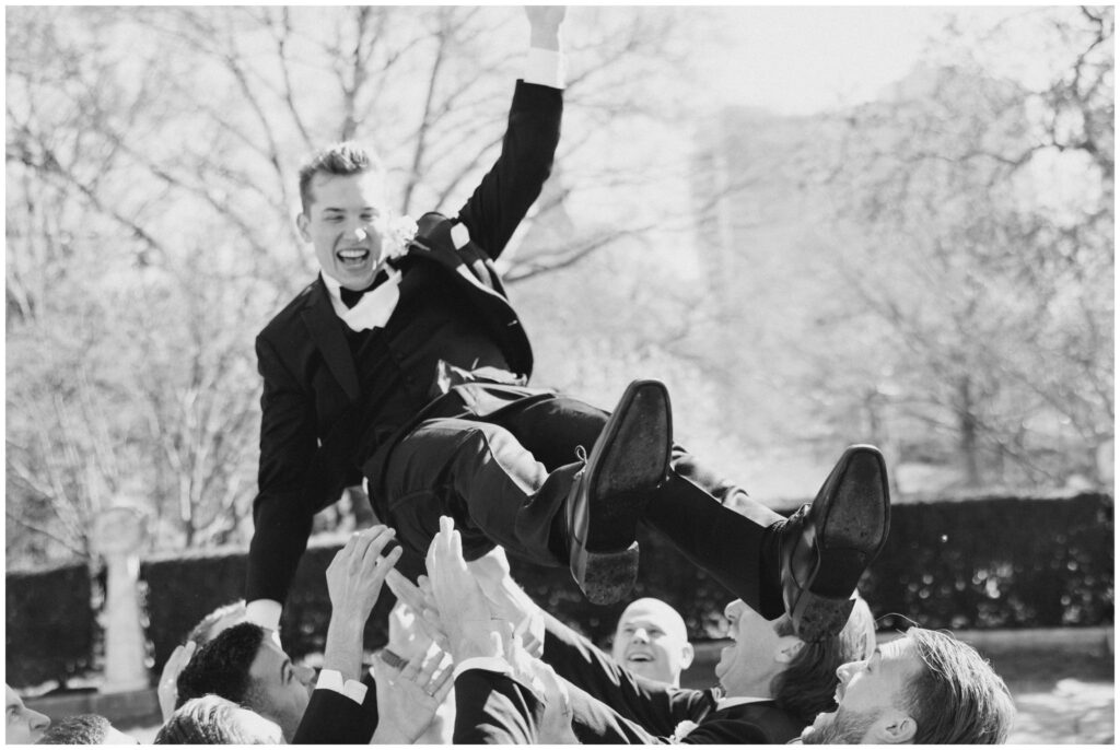 Groom being tossed in the air by his groomsmen